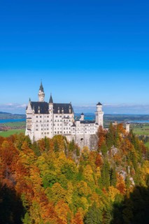 The fairytale Neuschwanstein Castle towers over an autumnal forest in front of vast landscapes,