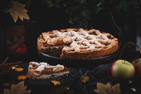 Icing sugar falls on apple pie surrounded by autumn leaves in a dark environment