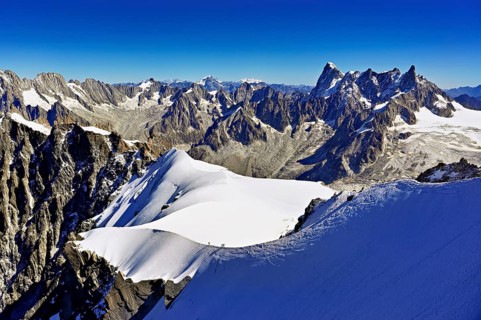 Mountaineers climb over a snow-covered ridge with Grandes Jorasses mountain in the background,