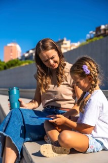 Mother and daughter smiling, sitting together on steps enjoying time outdoors, holding a reusable