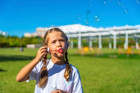 Child with pigtails enjoying summer playtime outdoors, actively creating and watching soap bubbles