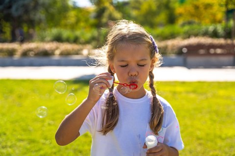 Little girl enjoying outdoor activity, blowing iridescent soap bubbles, experiencing joy and