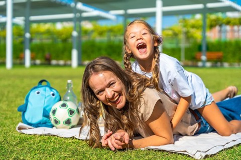 Mother and daughter bonding and having fun at a picnic in the park, the child playfully riding on