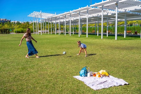 Mother and daughter playing soccer in a sunny green park, enjoying a picnic with blanket and