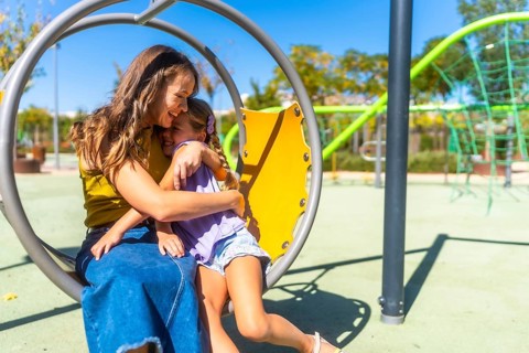 Mother and daughter share a warm hug and bright smiles on a sunny playground, enjoying playful