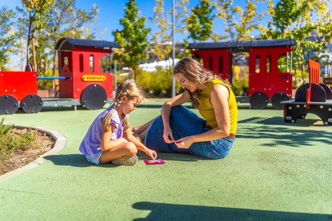 Mother and daughter bonding outdoors, sitting on the soft playground surface and concentrating on