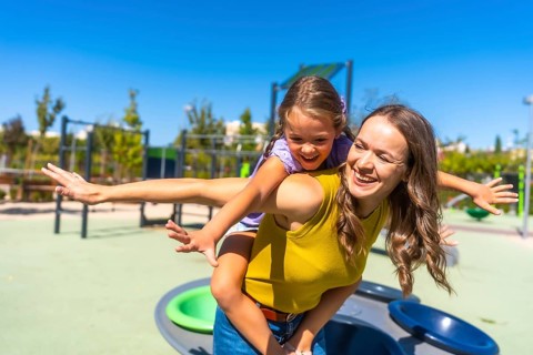 Happy mother giving her laughing daughter a piggyback ride on a sunny day in a modern public