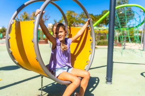 Young girl smiling on a modern oversized swing at a sunny outdoor playground, enjoying carefree