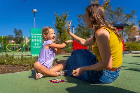 Mother and daughter sitting on playground ground, smiling and exchanging a joyful high five while