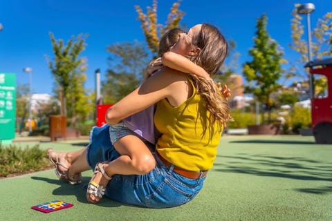 Mother and daughter embracing with affection on a soft ground surface at an outdoor playground,