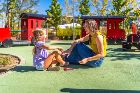 Mother and daughter sitting on soft flooring at a public playground, laughing happily during a