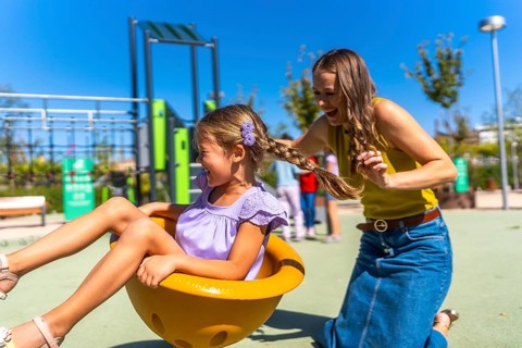Mother and daughter laughing on a sunny playground spinner, sharing carefree bonding and joyful