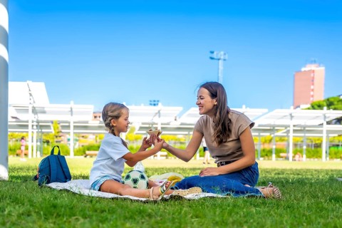 Mother and daughter spending quality time together on a picnic blanket in a sunny park, sharing a