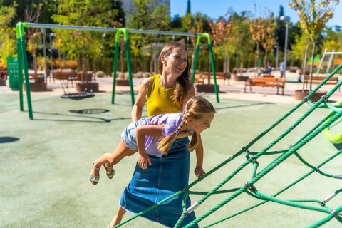 Mother and daughter smiling and laughing while playing on a sunny outdoor playground, climbing rope
