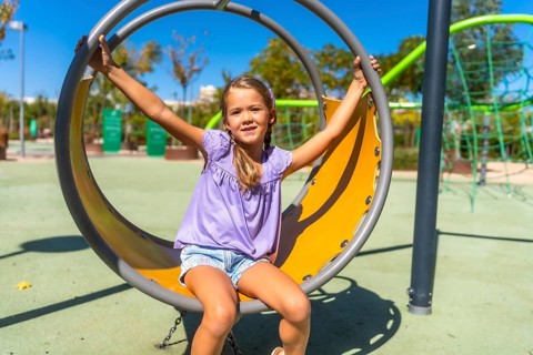 Happy child swinging on a round playground swing, enjoying outdoor activity on a sunny day,