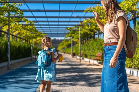 Woman and young girl walking along a path surrounded by lush green foliage and a modern pergola, a