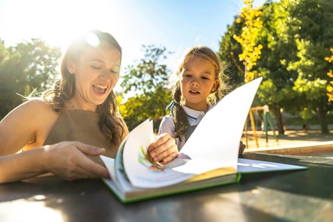 Mother and daughter engaging in a fun reading activity, turning pages of a colorful book while