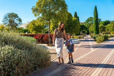 Mother and daughter walking along a path in a park, holding hands and going to school on a sunny