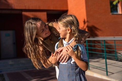 Woman tenderly hugging her daughter wearing a school uniform, sharing a loving moment outside the