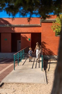 Mother and daughter holding hands and walking together, approaching a school building on a sunny