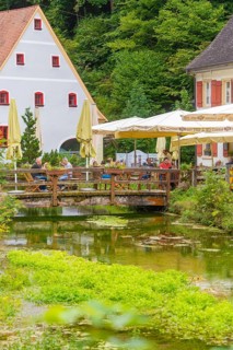 People sitting in a café by a stream in picturesque landscape, Wimsener Höhle, Hayingen, Germany