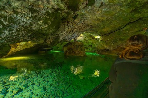 Interior of a cave with green water and rocks, people exploring the underground body of water,