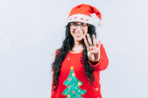 Happy girl in Christmas hat counting number FOUR, isolated. Smiling girl in Christmas sweater