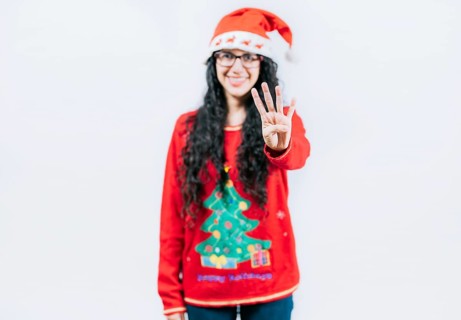 Smiling girl in Christmas sweater counting number 4. Happy girl in Christmas hat counting number