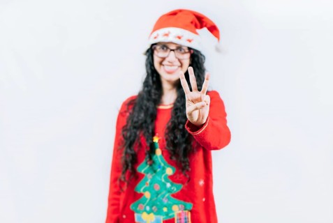 Happy girl in Christmas hat counting number THREE, isolated. Smiling girl in Christmas sweater