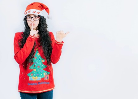 Girl in Christmas sweater and glasses pointing to the side, isolated. Young woman in Christmas hat