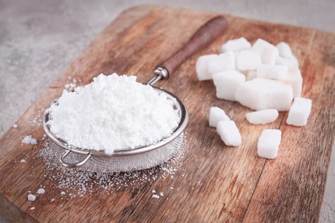 A strainer with powdered sugar, on a wooden cutting board, with pieces of white sugar