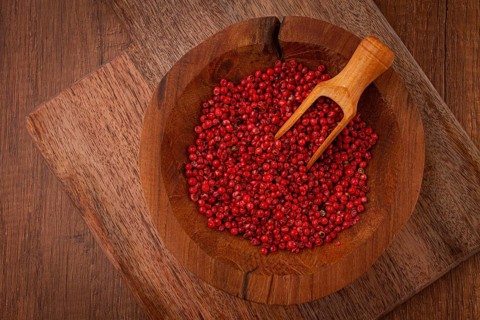 Bright red peppercorns, in a wooden bowl, with a small wooden tray