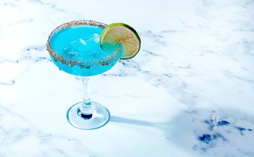 Bright blue cocktail with a slice of lime on a marble surface
