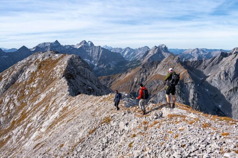 Hikers on the summit ridge of the Gamsjoch, behind rock faces of the Laliderer Spitze, eastern