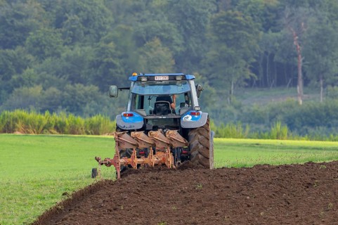 Tractor with plough, agricultural ploughing machine working on a field in autumn, fall in the