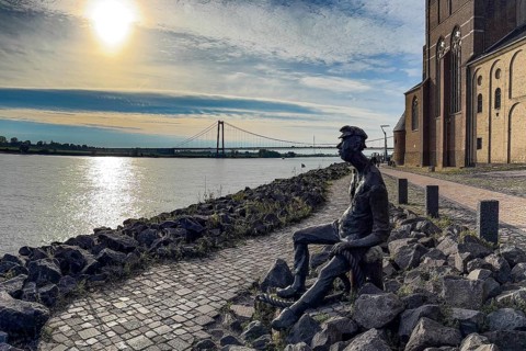 Photo with melancholy mood of bronze sculpture Poortekerl looking at Rhine waiting for ship to