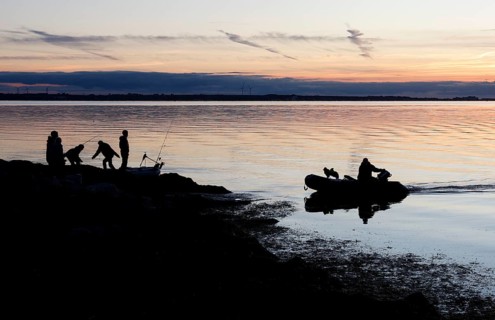 Angler on the beach during sunset, an angler docks on the shore with his inflatable boat and dog,