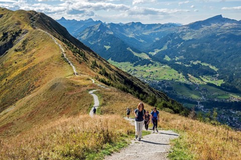 Hikers on the Fellhorn ridge hiking trail, behind Kleinwalsertal with mountains of the Allgäu Alps,