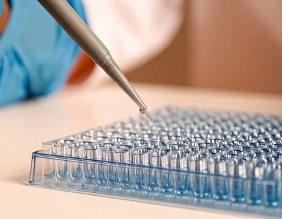 Controlled droplet from a pipette over rows of clear wells on a blue plate, Pipette dispensing a