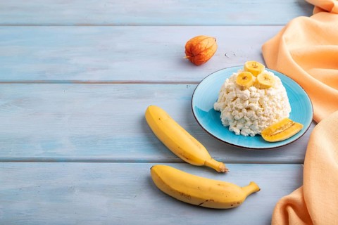 White ?ottage cheese, Curd, with Banana on blue wooden background and orange textile, side view,