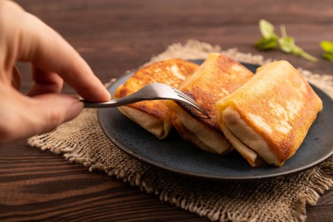 Fried crispy pancakes with meat and cheese with hand on brown wooden background and linen textile.
