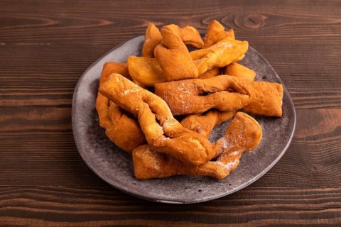 Crunchy biscuit Brushwood cookies sprinkled with powdered sugar on brown wooden background, side