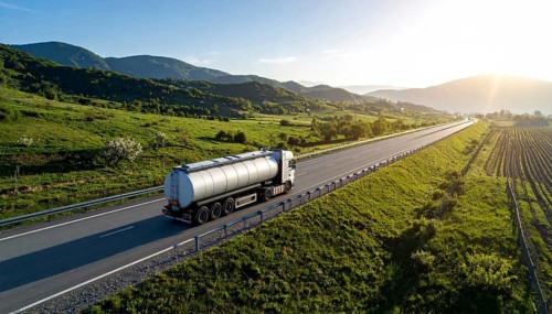 Petrol cargo truck lorry tanker driving on highway hauling oil products at sunrise, wide hilly