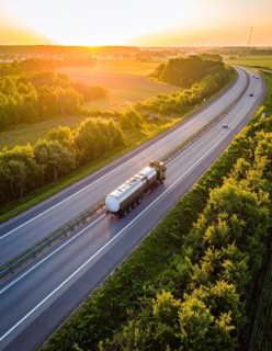 Petrol cargo truck lorry tanker driving on highway hauling oil products at sunrise, wide hilly