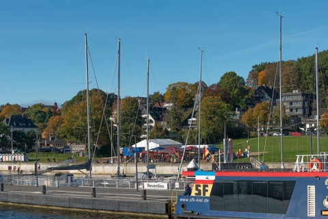 Kiel harbour, Kiellinie waterfront, Reventlou pier, restaurant, ferry, trees in autumn colors, blue