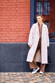 A fashionable woman stands confidently against a vibrant red brick wall. She wears a stylish long