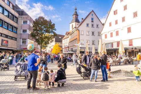 Bustling market square with families, church in the background, sunny day and historic houses,