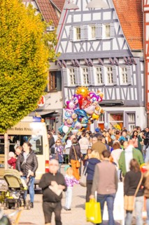 People pass half-timbered houses, colorful balloons over a lively crowd of roads, Urschelherbst
