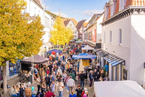 A long market street full of people in autumn surrounded by half-timbered houses and yellow trees,