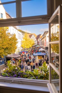 From a window you can see a lively street full of people and colorful market stalls under yellow